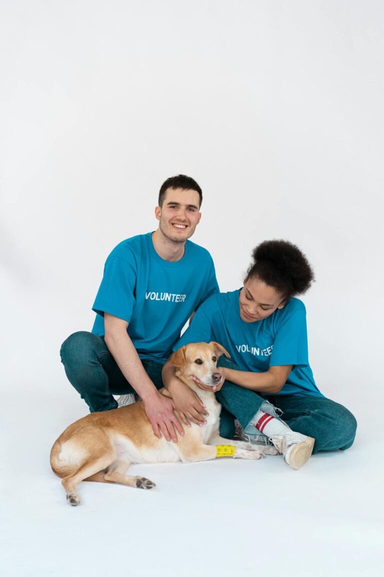 A diverse group of volunteers posing happily with a cute dog in a bright studio setting.