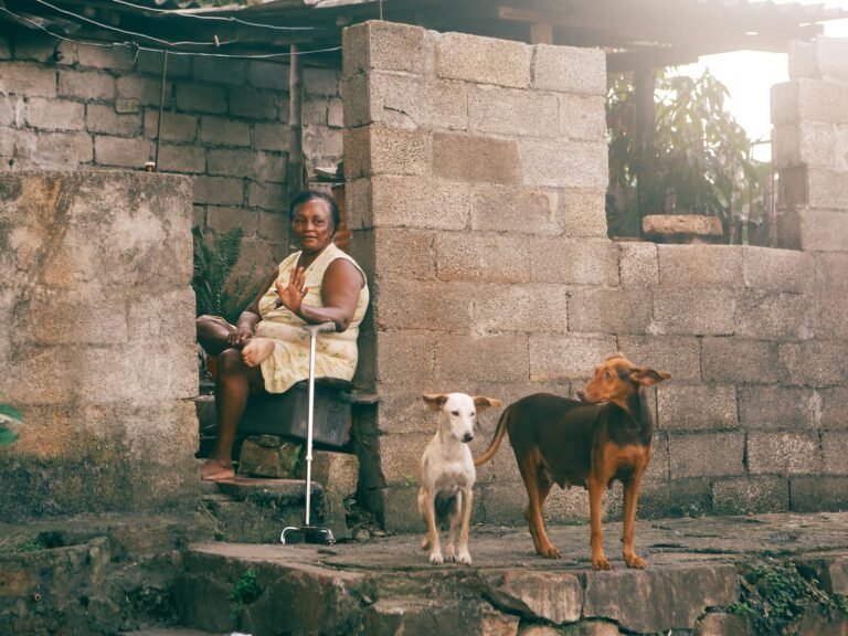 Senior woman sitting with her dogs outside her home in a rustic setting.