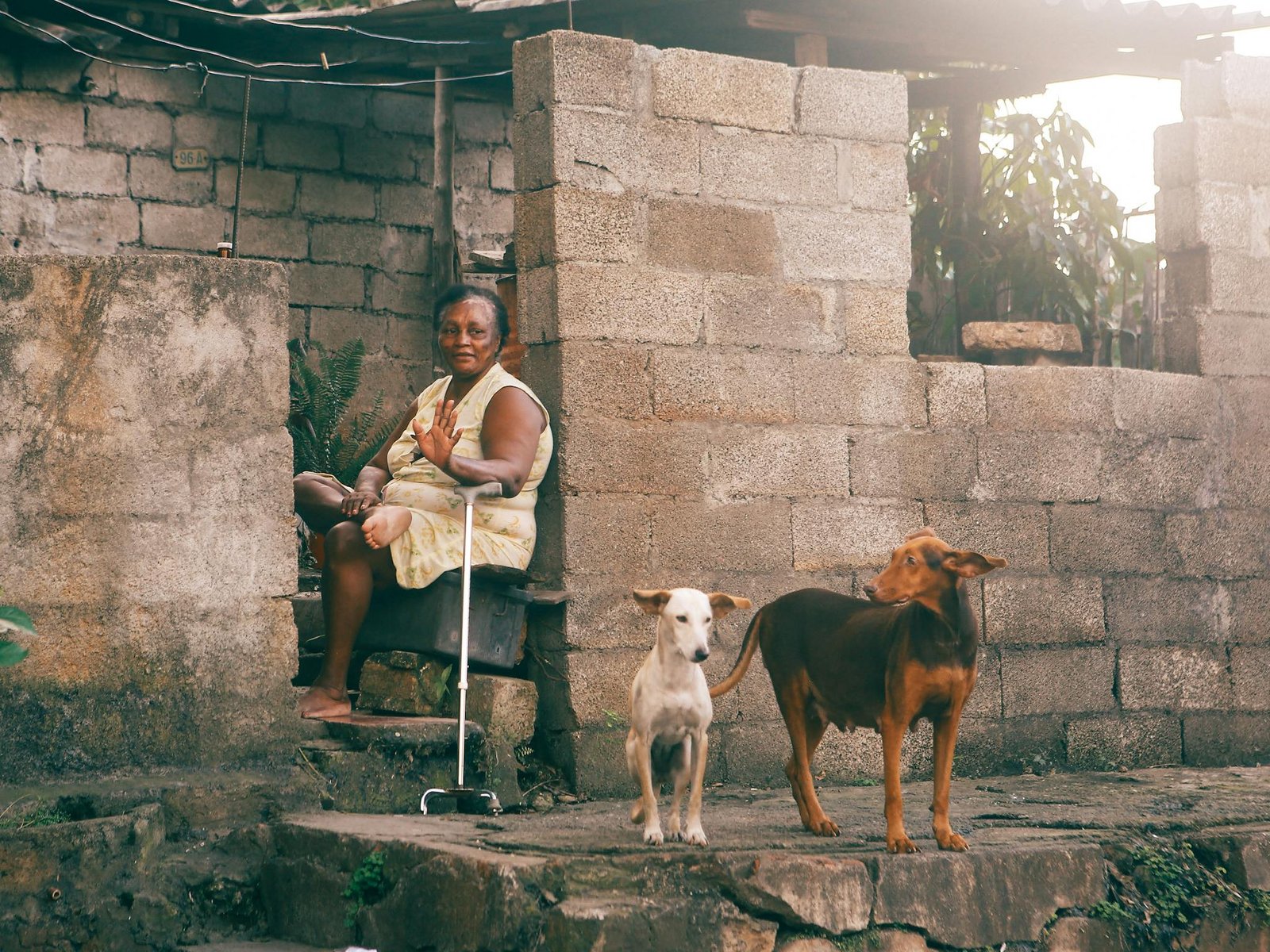 Senior woman sitting with her dogs outside her home in a rustic setting.