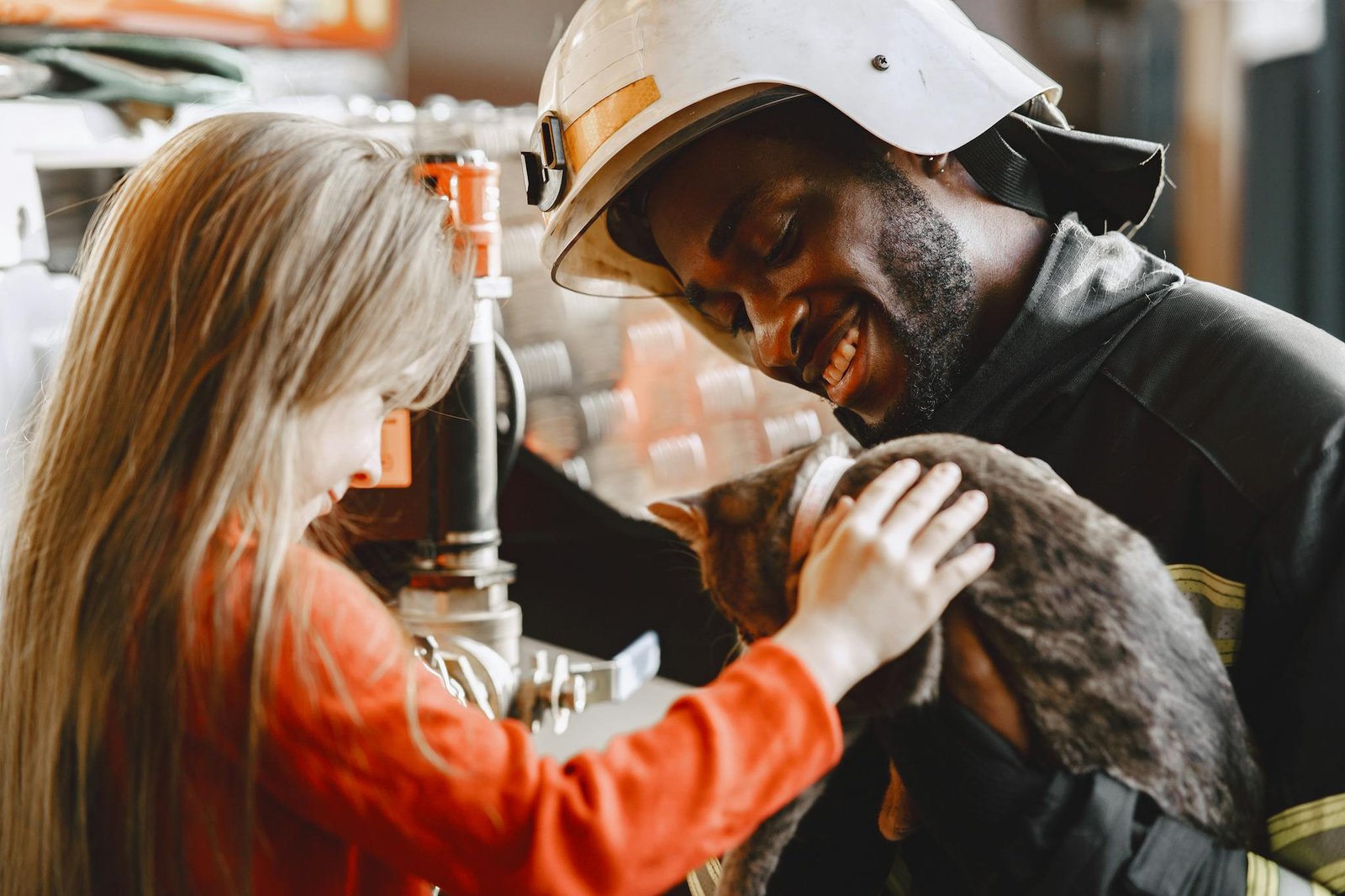 Smiling firefighter and child petting a cat indoors, creating a warm and joyful scene.